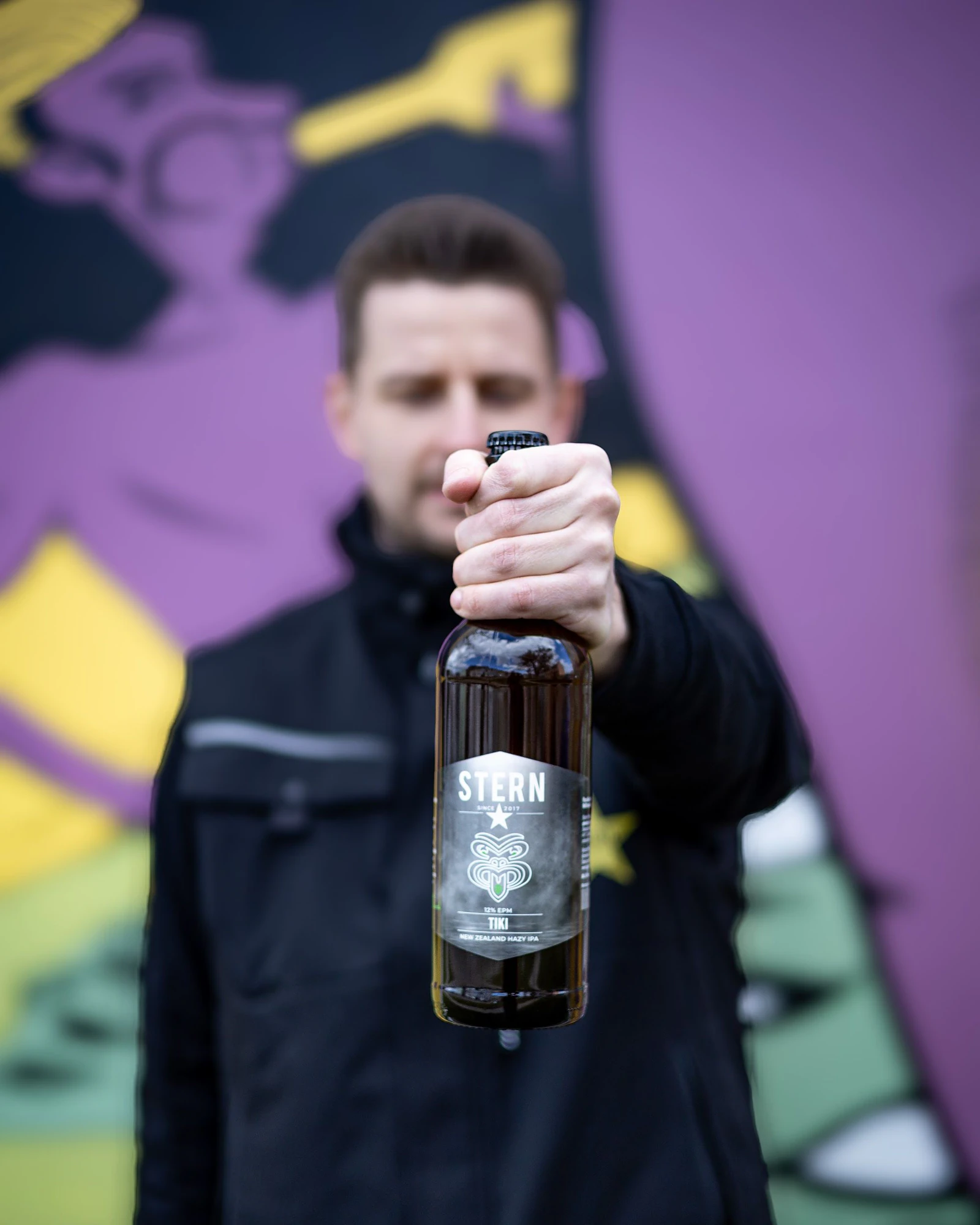 Člen týmu Stern drží lahev piva před graffiti